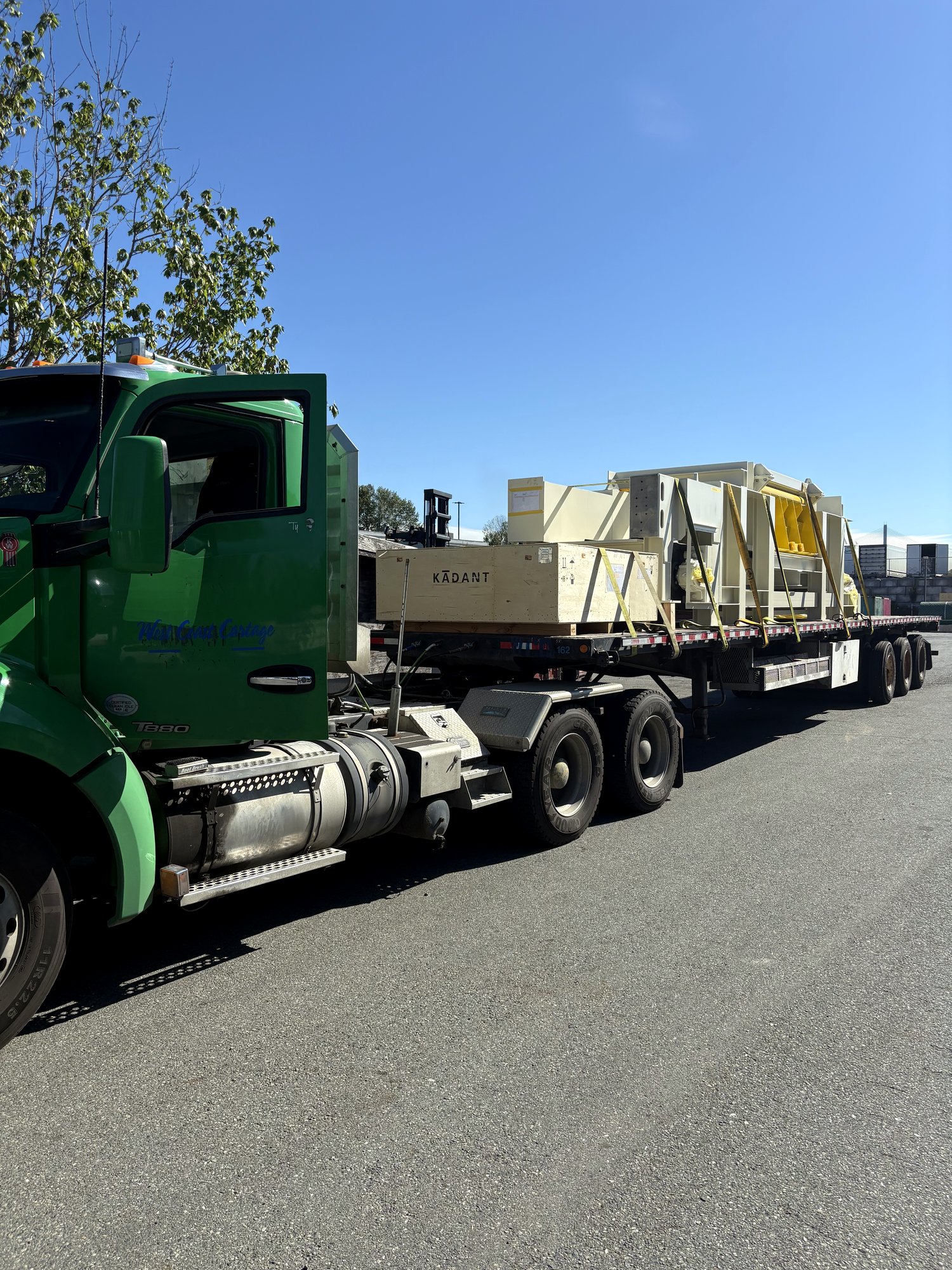 A West Coast Cartage flatbed loaded with crated industrial equipment, double-drop deck